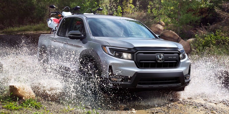 Honda Ridgeline TrailSport crossing mountain stream with dirt bike in bed